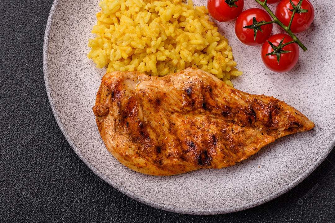 Delicioso filé de frango grelhado fresco com especiarias e ervas em um fundo escuro de concreto. Um prato cozido no fogo