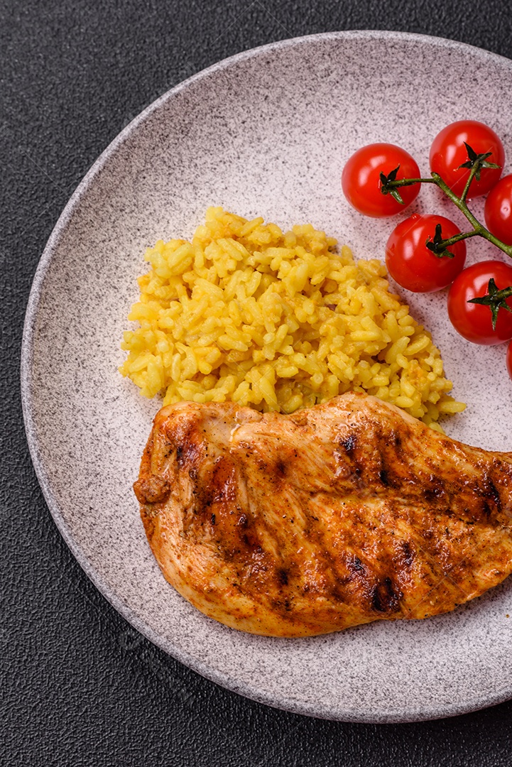 Delicioso filé de frango grelhado fresco com especiarias e ervas em um fundo escuro de concreto. Um prato cozido no fogo