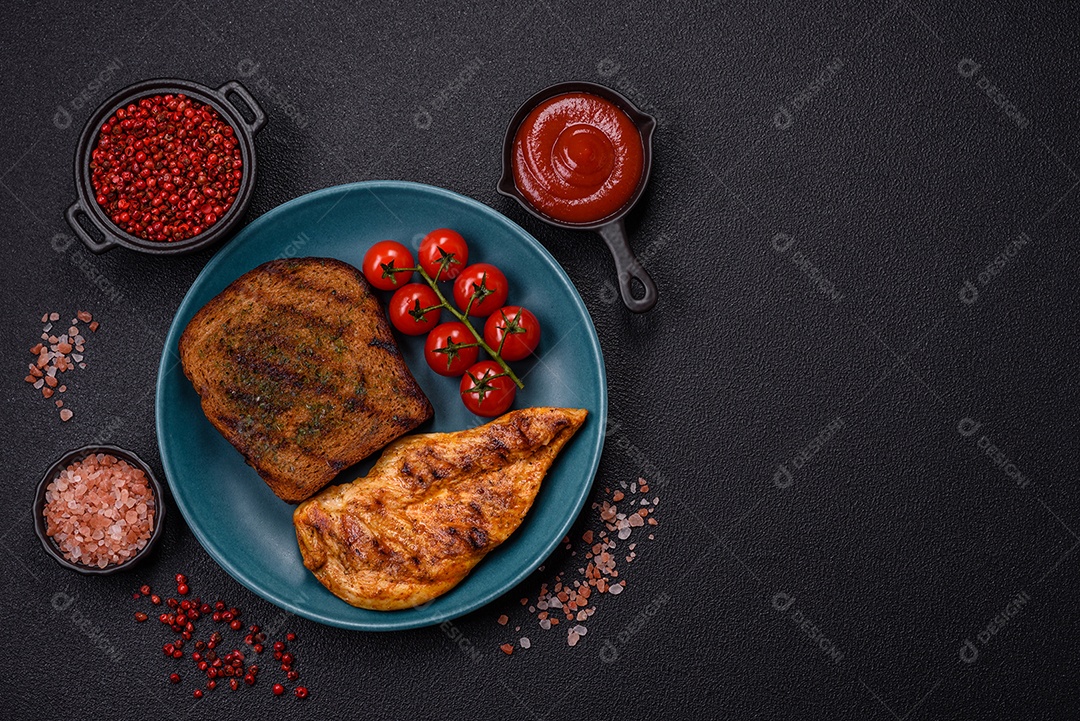 Delicioso filé de frango grelhado fresco com especiarias e ervas em um fundo escuro de concreto. Um prato cozido no fogo