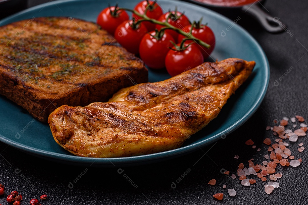 Delicioso filé de frango grelhado fresco com especiarias e ervas em um fundo escuro de concreto. Um prato cozido no fogo