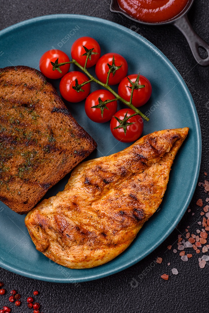 Delicioso filé de frango grelhado fresco com especiarias e ervas em um fundo escuro de concreto. Um prato cozido no fogo