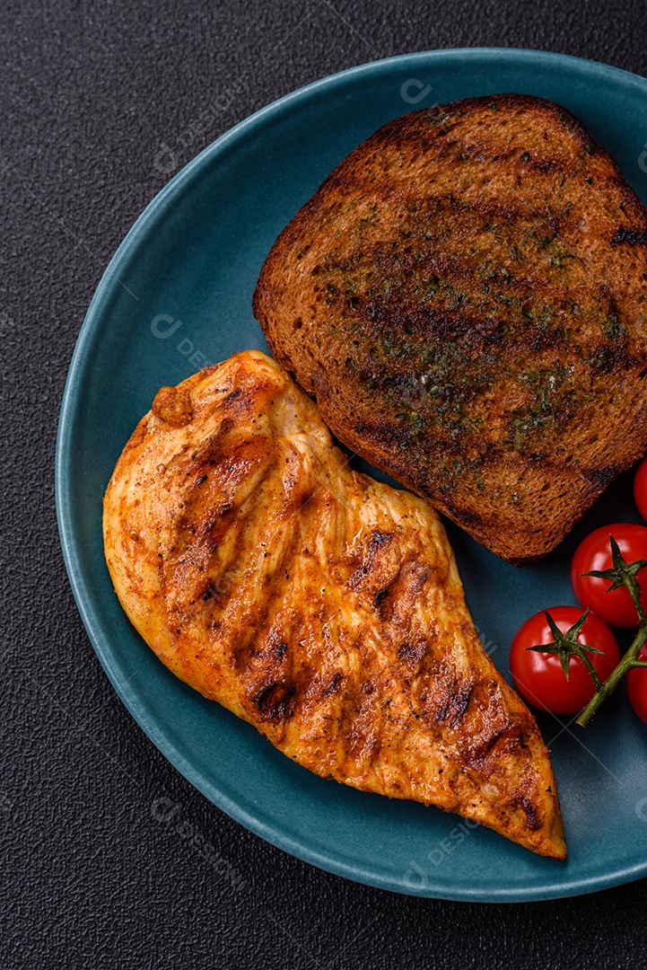 Delicioso filé de frango grelhado fresco com especiarias e ervas em um fundo escuro de concreto. Um prato cozido no fogo