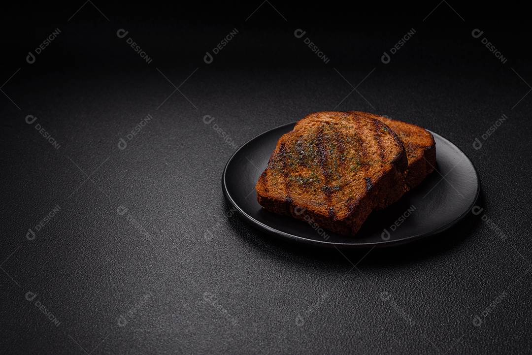 Deliciosos croutons crocantes ou bruschetta de pão integral com molho de alho e ervas sobre um fundo escuro de concreto