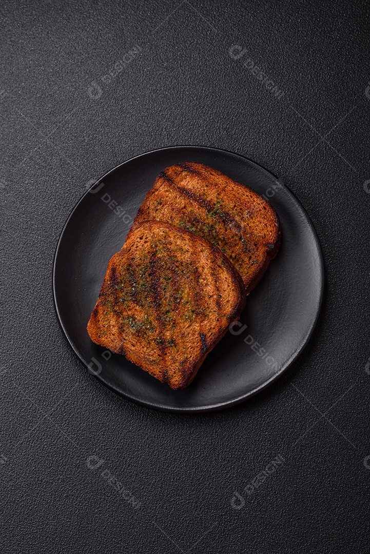 Deliciosos croutons crocantes ou bruschetta de pão integral com molho de alho e ervas sobre um fundo escuro de concreto