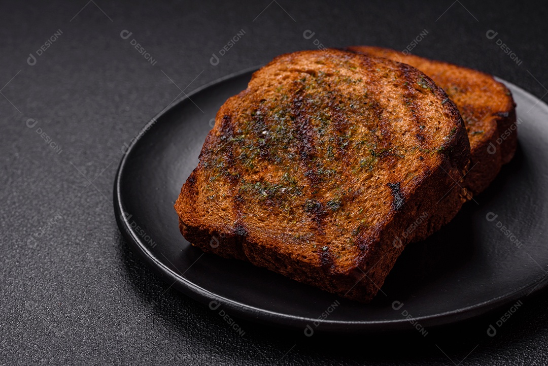 Deliciosos croutons crocantes ou bruschetta de pão integral com molho de alho e ervas sobre um fundo escuro de concreto