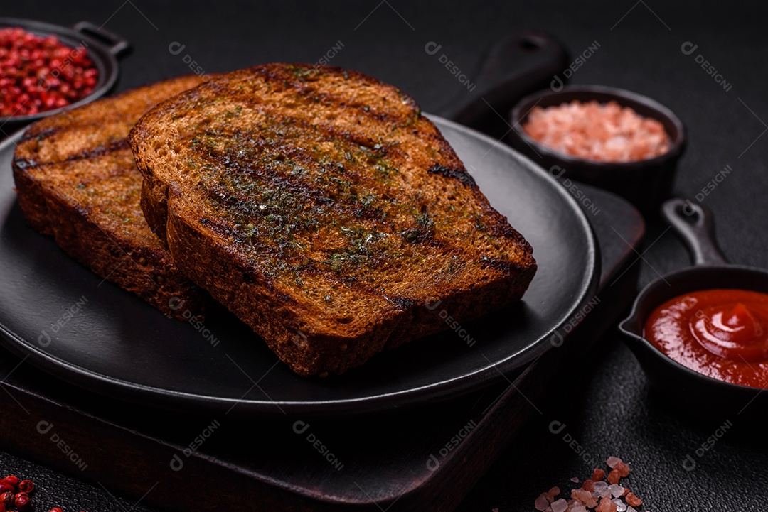 Deliciosos croutons crocantes ou bruschetta de pão integral com molho de alho e ervas sobre um fundo escuro de concreto