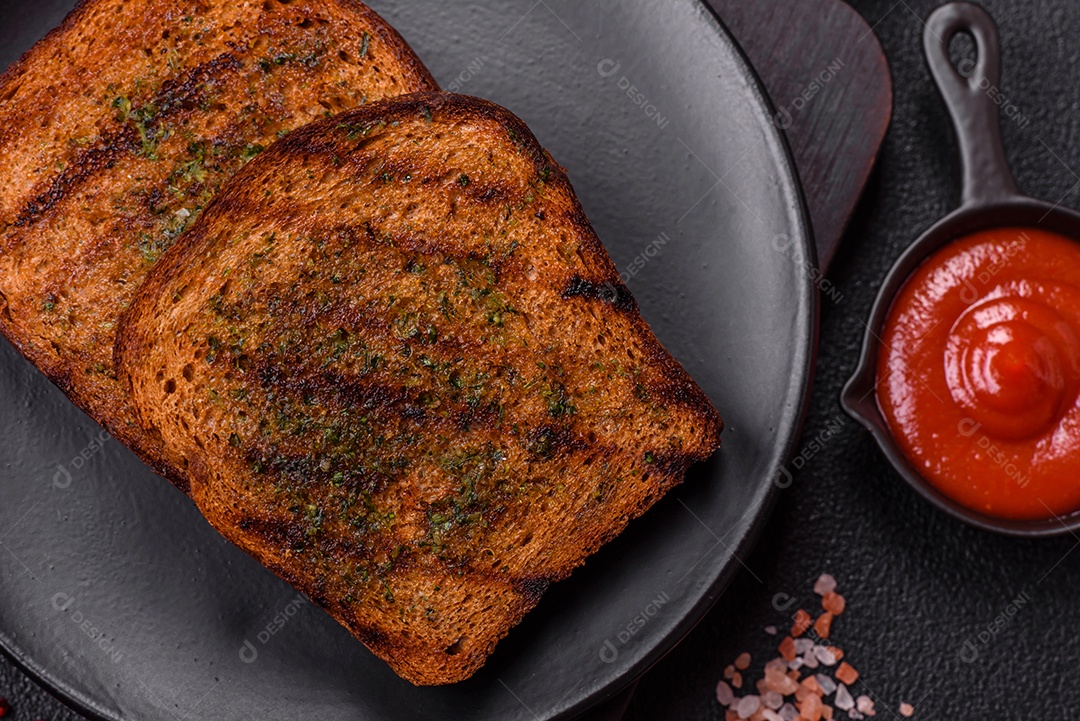 Deliciosos croutons crocantes ou bruschetta de pão integral com molho de alho e ervas sobre um fundo escuro de concreto