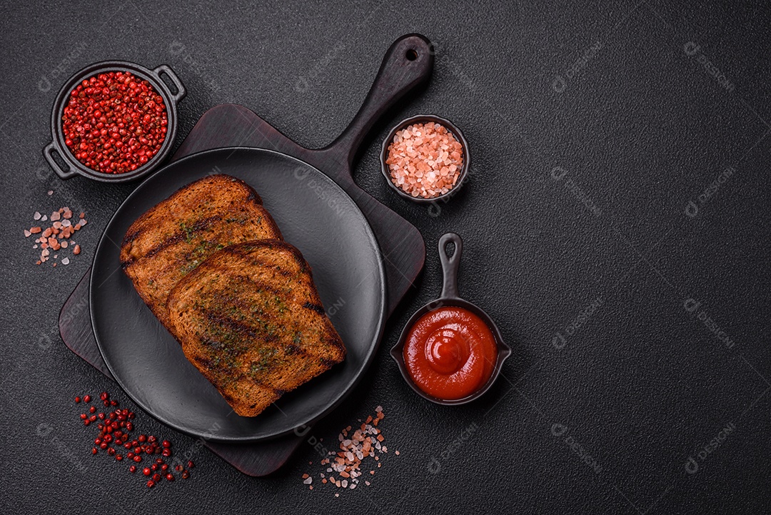 Deliciosos croutons crocantes ou bruschetta de pão integral com molho de alho e ervas sobre um fundo escuro de concreto