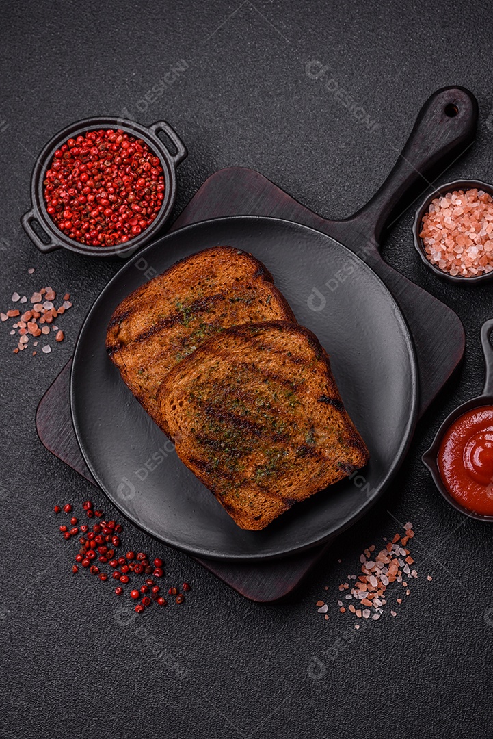 Deliciosos croutons crocantes ou bruschetta de pão integral com molho de alho e ervas sobre um fundo escuro de concreto