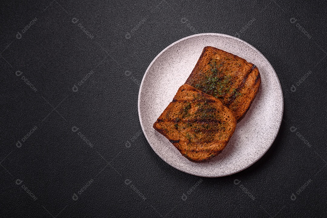 Deliciosos croutons crocantes ou bruschetta de pão integral com molho de alho e ervas sobre um fundo escuro de concreto