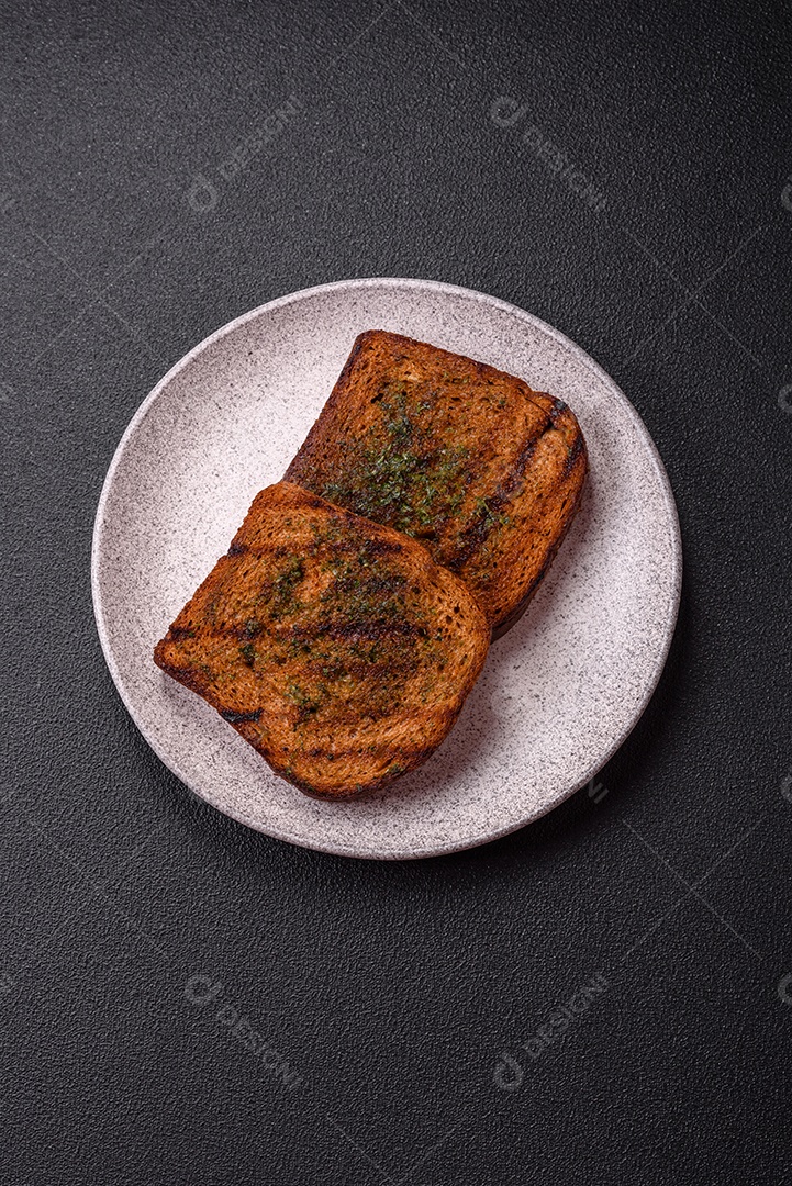 Deliciosos croutons crocantes ou bruschetta de pão integral com molho de alho e ervas sobre um fundo escuro de concreto
