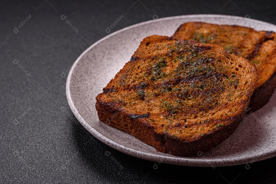 Deliciosos croutons crocantes ou bruschetta de pão integral com molho de alho e ervas sobre um fundo escuro de concreto