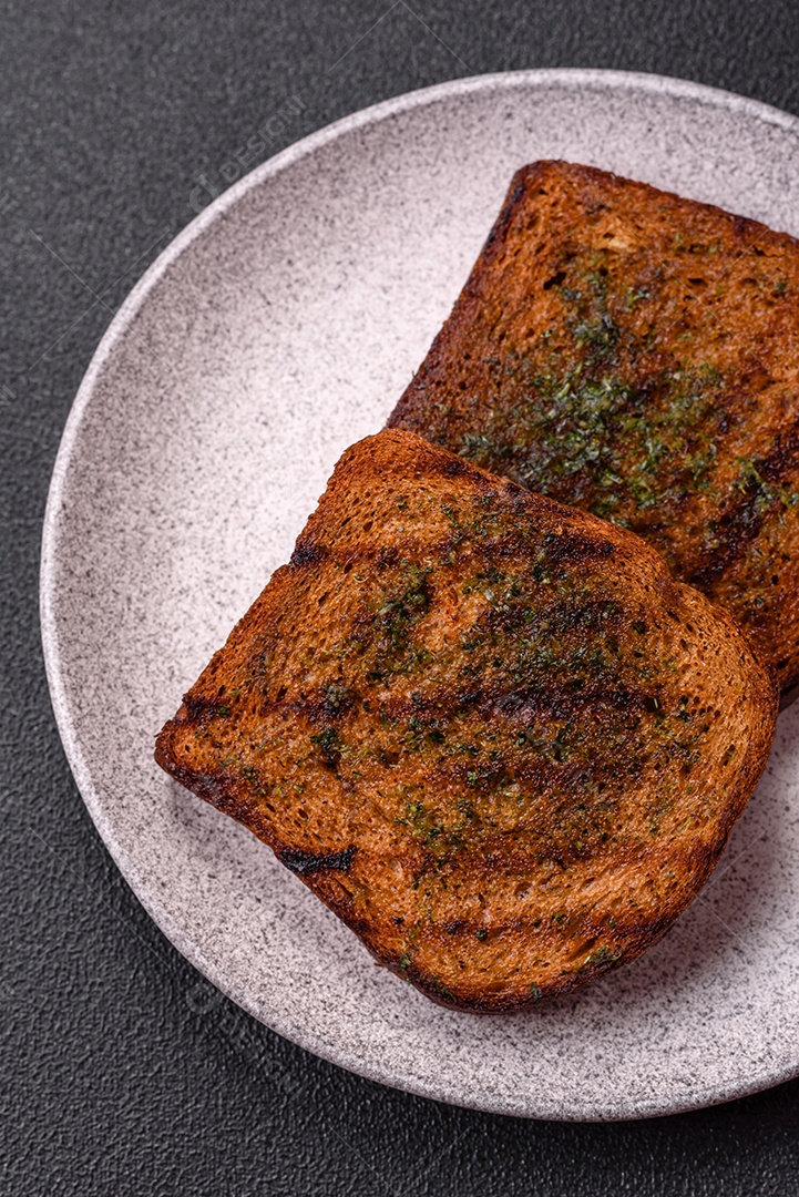 Deliciosos croutons crocantes ou bruschetta de pão integral com molho de alho e ervas sobre um fundo escuro de concreto