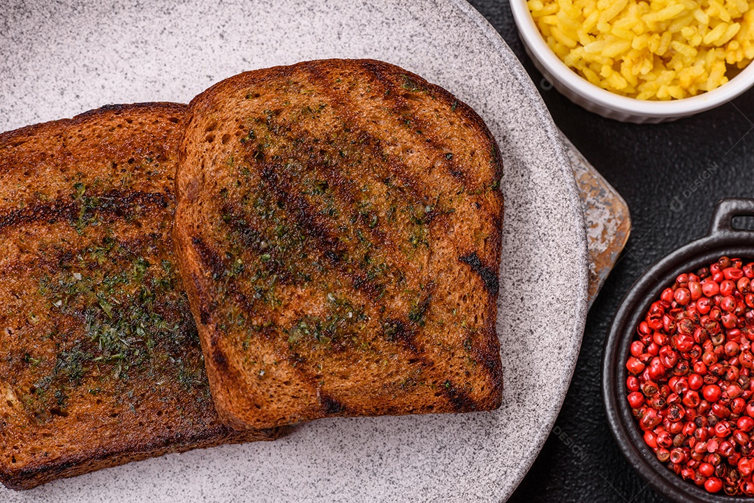 Deliciosos croutons crocantes ou bruschetta de pão integral com molho de alho e ervas sobre um fundo escuro de concreto