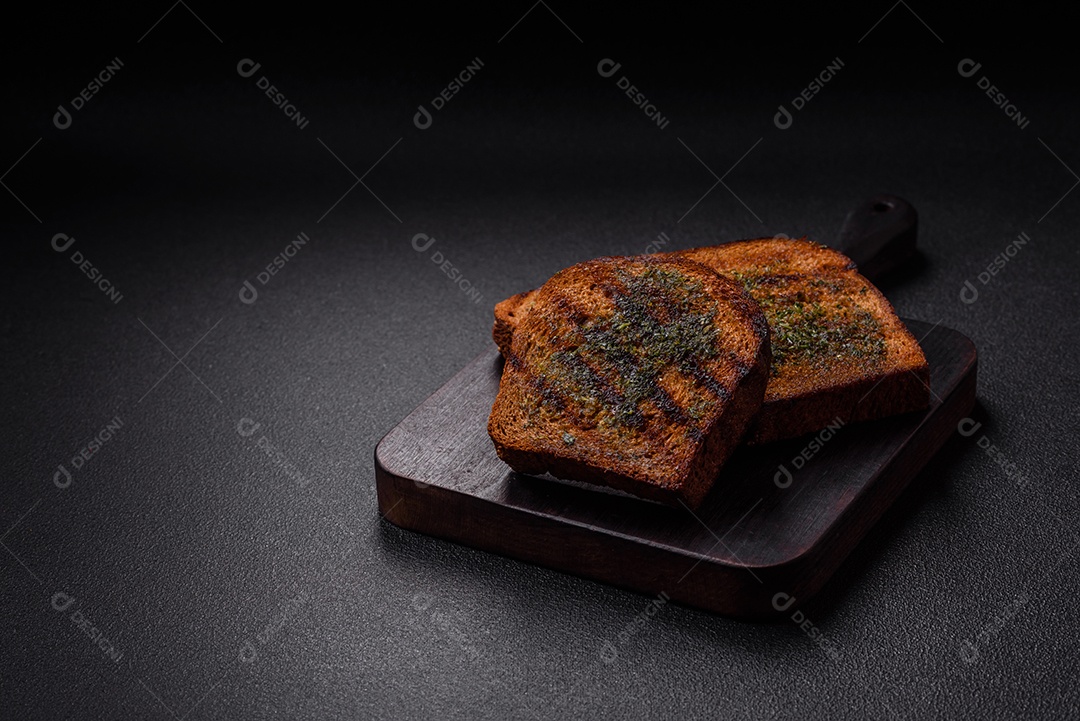 Deliciosos croutons crocantes ou bruschetta de pão integral com molho de alho e ervas sobre um fundo escuro de concreto