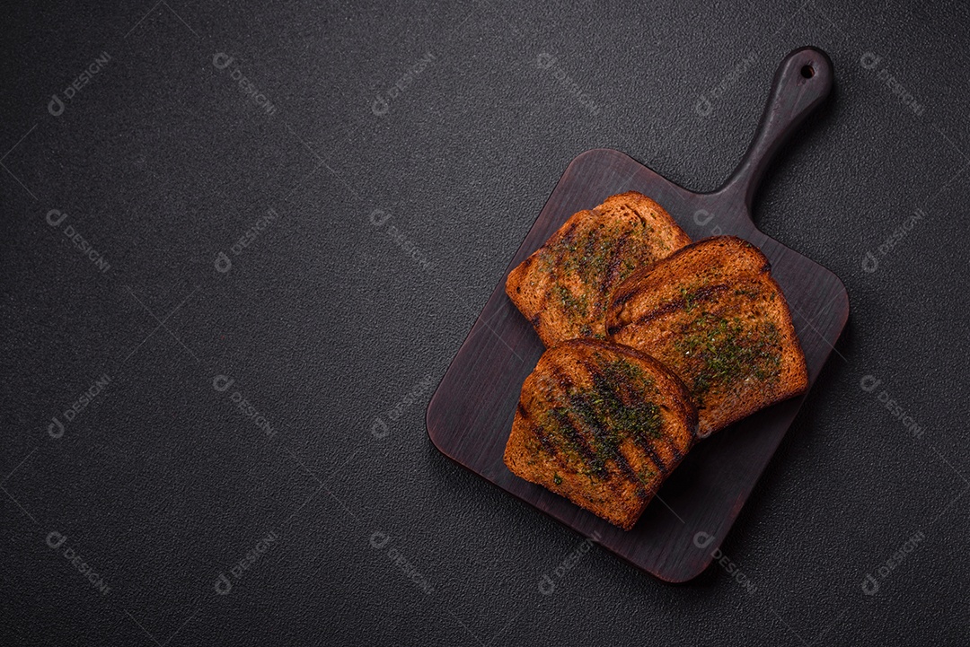 Deliciosos croutons crocantes ou bruschetta de pão integral com molho de alho e ervas sobre um fundo escuro de concreto