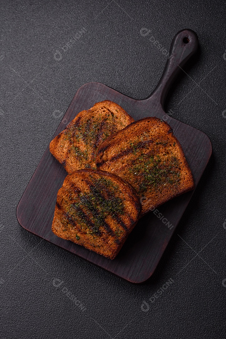 Deliciosos croutons crocantes ou bruschetta de pão integral com molho de alho e ervas sobre um fundo escuro de concreto