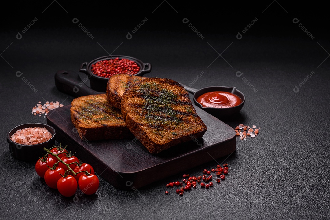 Deliciosos croutons crocantes ou bruschetta de pão integral com molho de alho e ervas sobre um fundo escuro de concreto