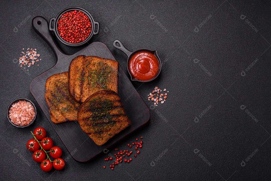 Deliciosos croutons crocantes ou bruschetta de pão integral com molho de alho e ervas sobre um fundo escuro de concreto