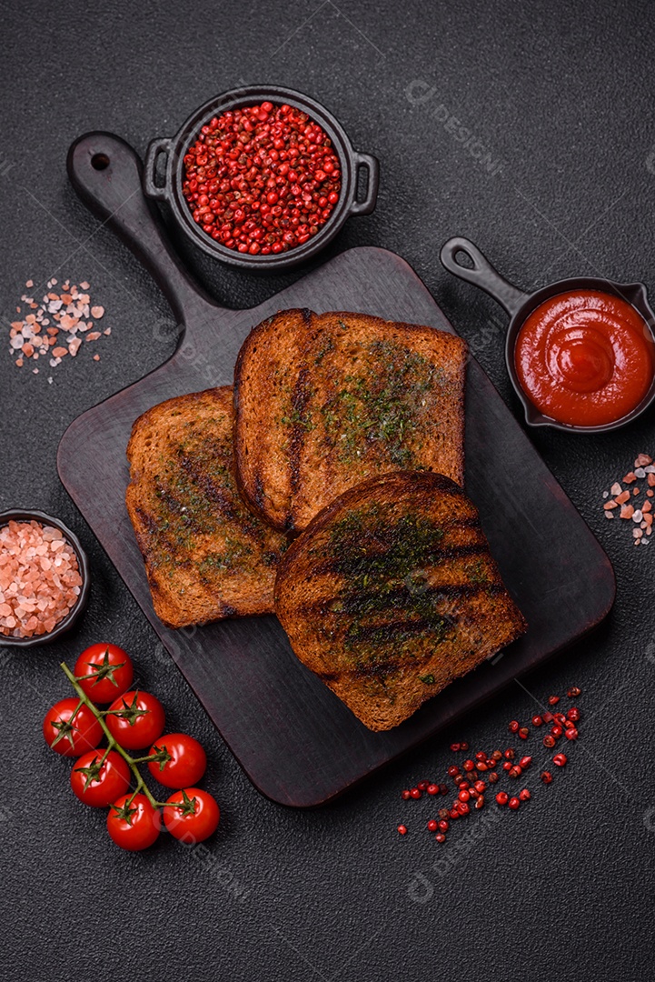 Deliciosos croutons crocantes ou bruschetta de pão integral com molho de alho e ervas sobre um fundo escuro de concreto