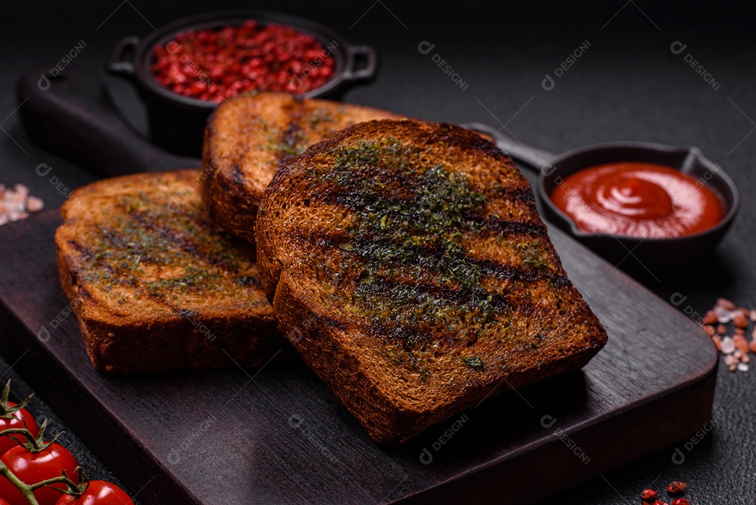 Deliciosos croutons crocantes ou bruschetta de pão integral com molho de alho e ervas sobre um fundo escuro de concreto