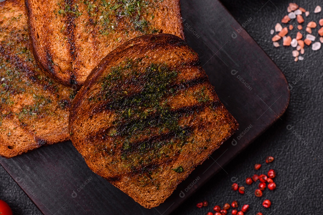 Deliciosos croutons crocantes ou bruschetta de pão integral com molho de alho e ervas sobre um fundo escuro de concreto
