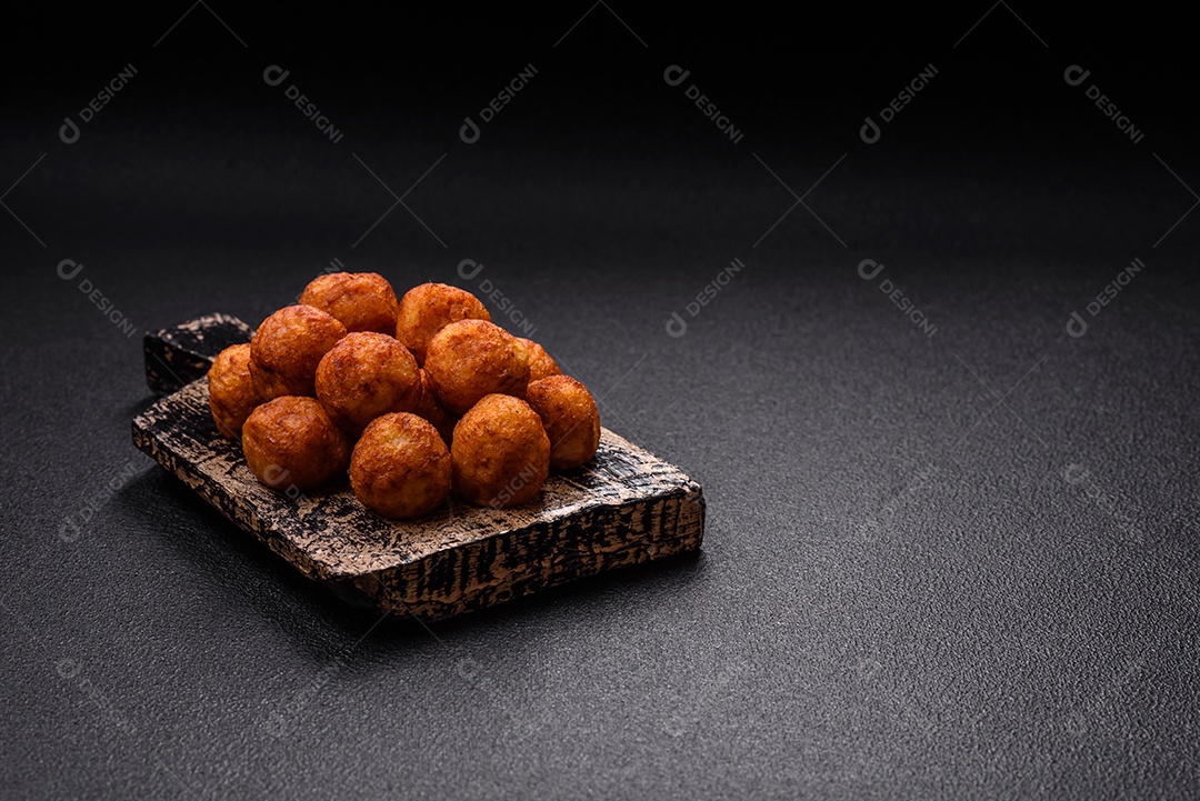 Deliciosas bolas crocantes empanadas com queijo mussarela, sal e especiarias em fundo escuro de concreto