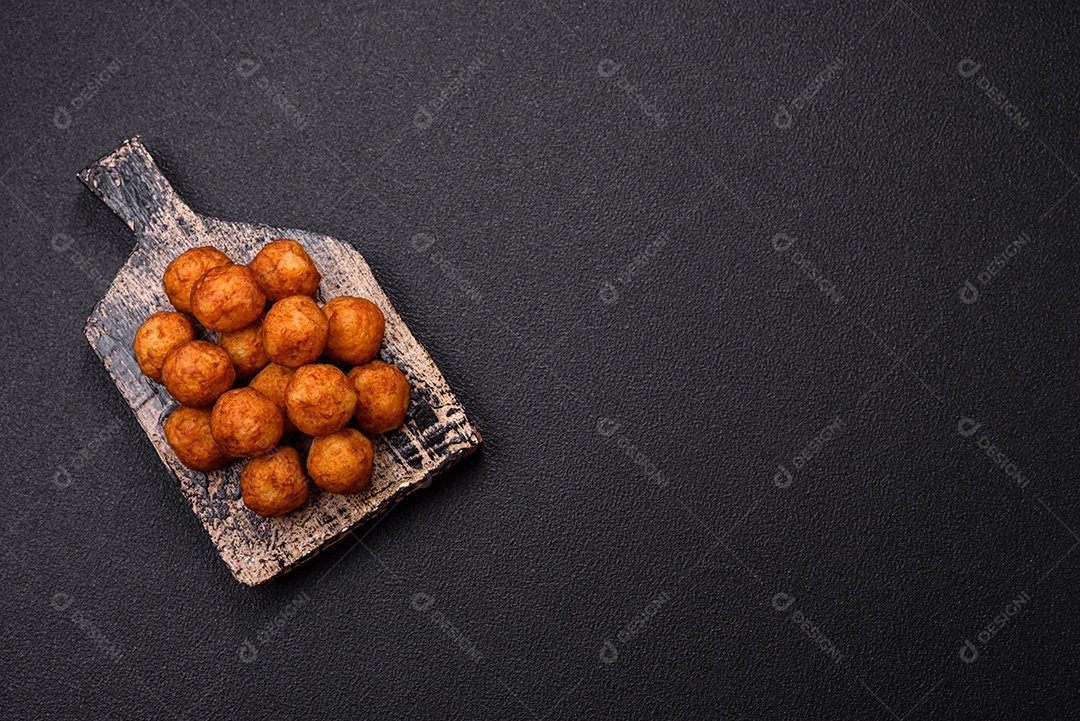 Deliciosas bolas crocantes empanadas com queijo mussarela, sal e especiarias em fundo escuro de concreto