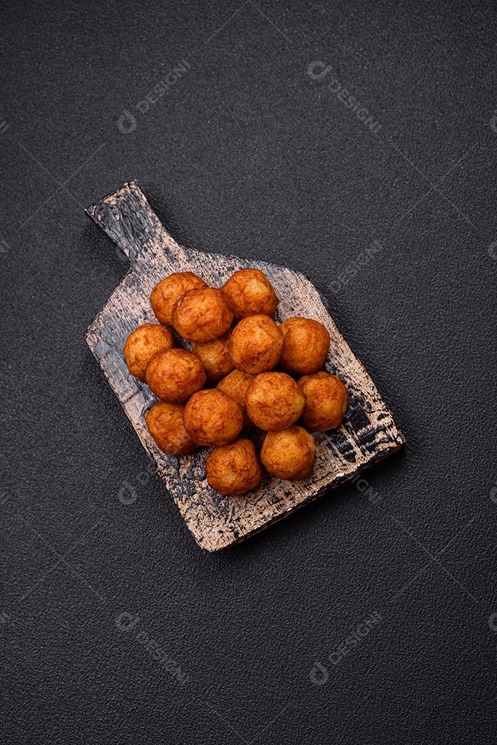 Deliciosas bolas crocantes empanadas com queijo mussarela, sal e especiarias em fundo escuro de concret