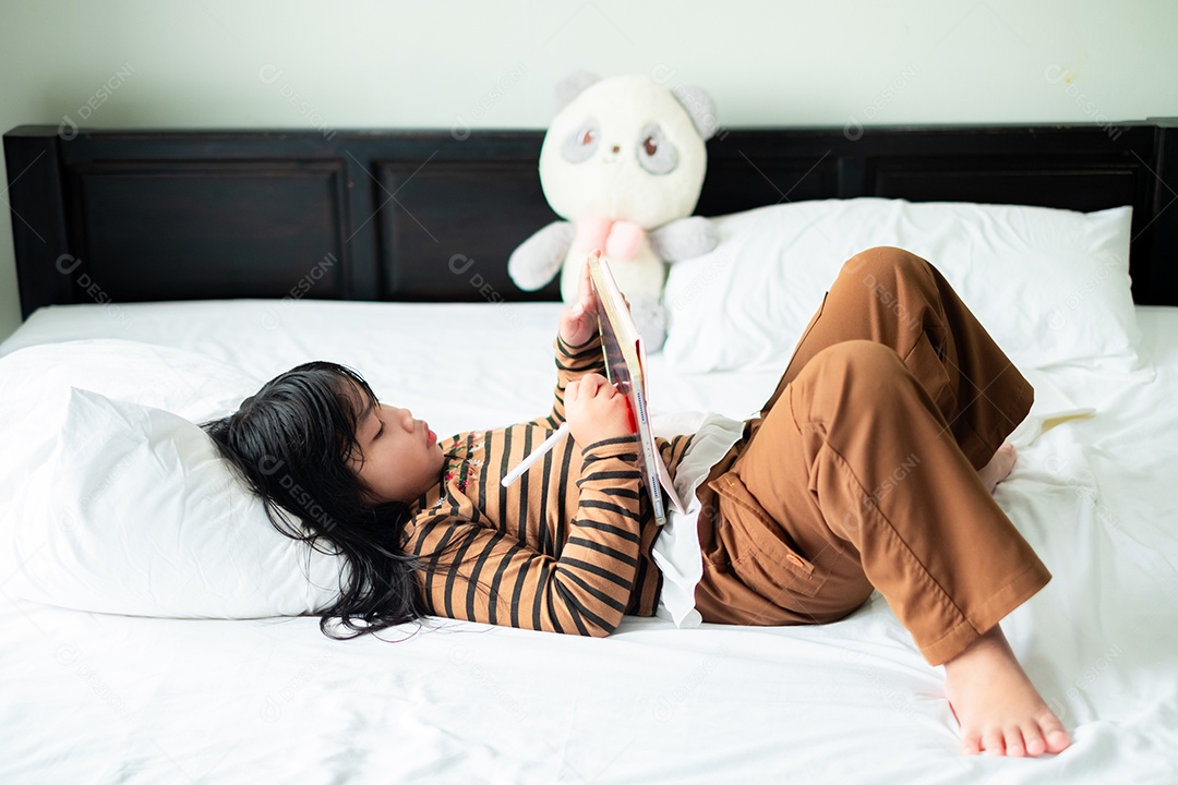 Linda garota asiática deitada e brincando com um tablet em um colchão branco macio