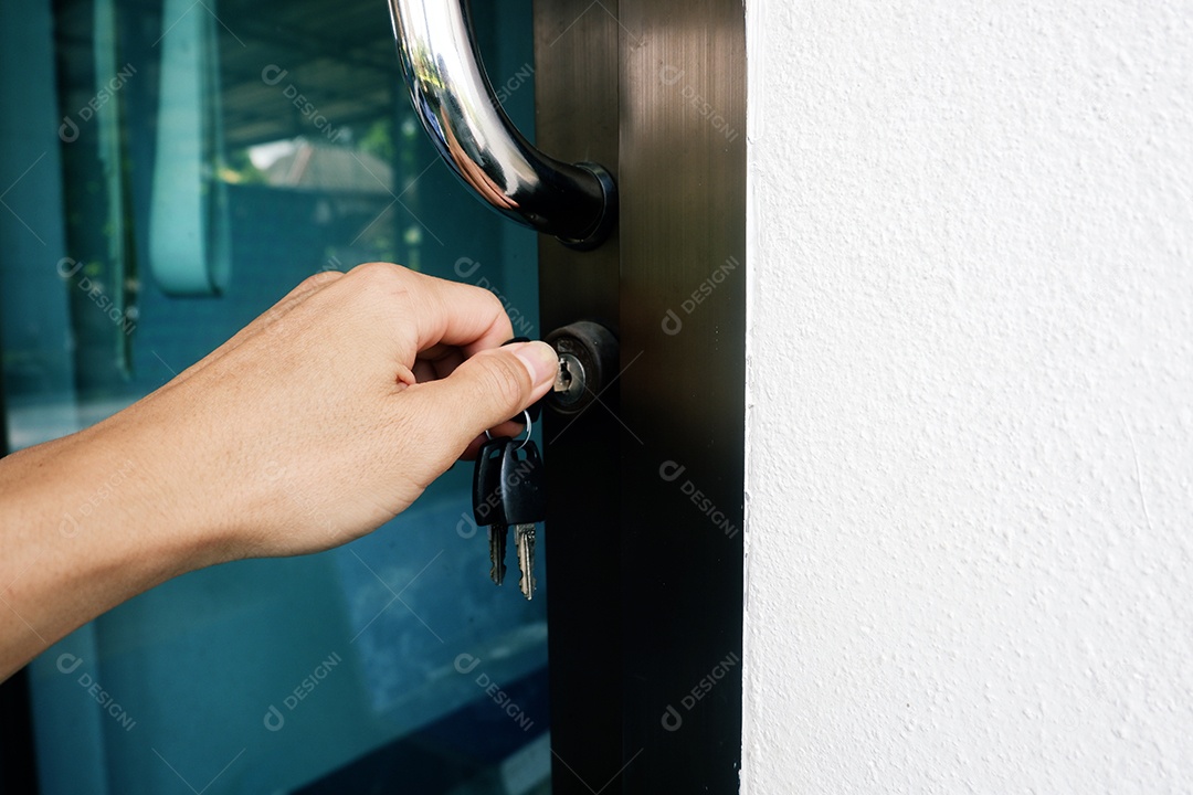 A mão de um homem segura uma chave e a gira para destrancar e abrir a porta