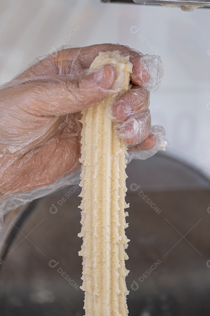 Mão segurando massa crua de churros para fritar