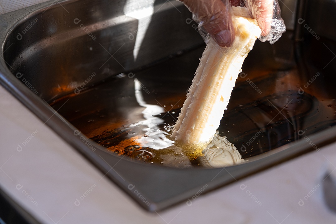 Mão colocando churros para fritar