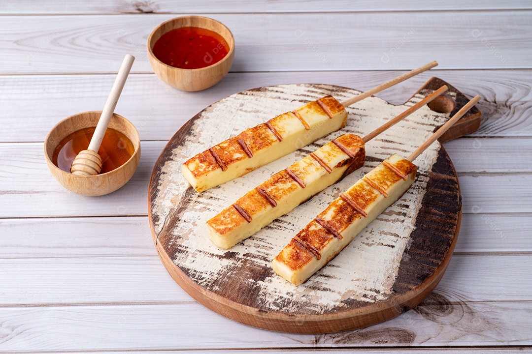 Tábua de madeira com espetinhos de queijo e molho na lateral