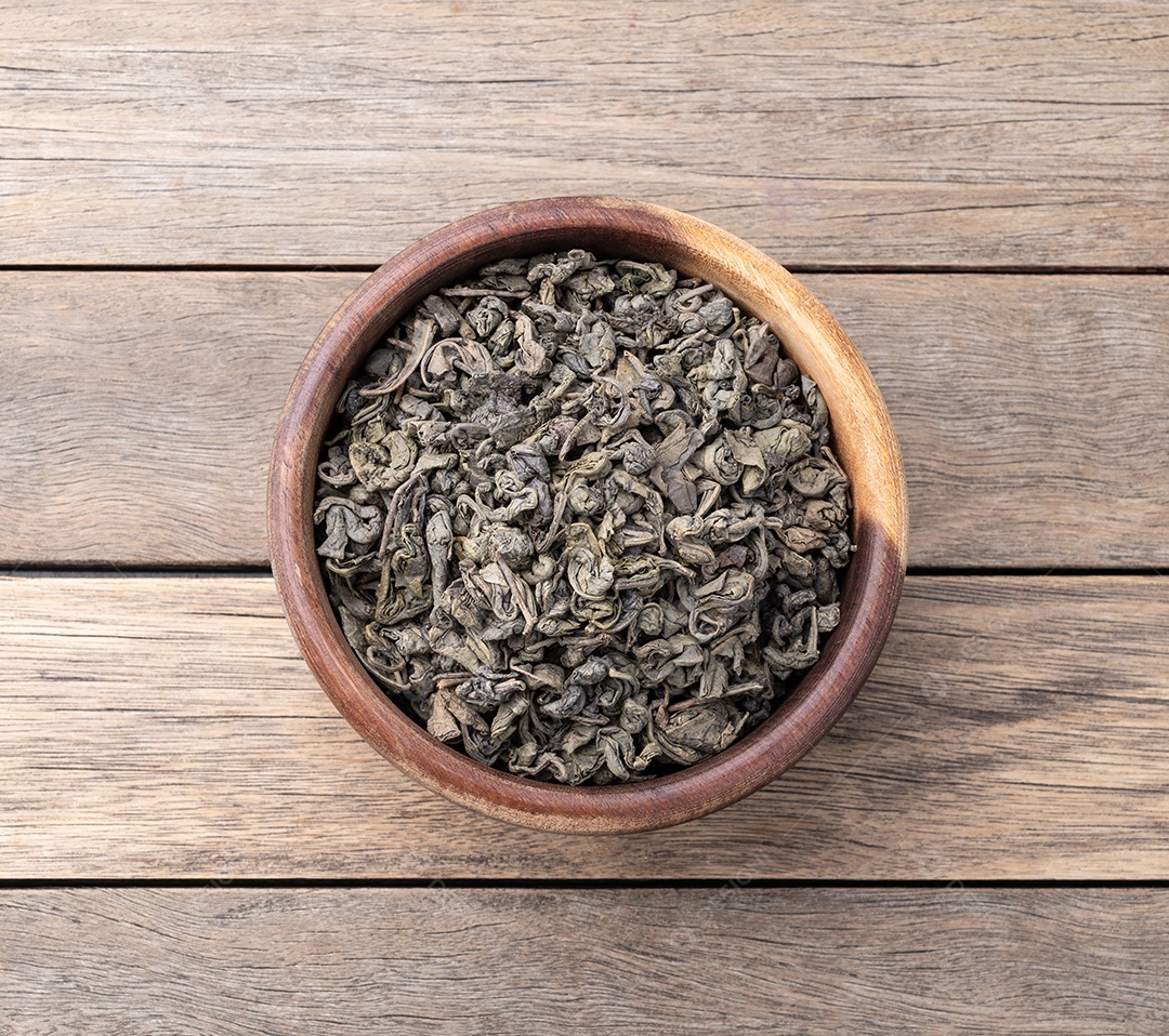 Folhas secas de chá verde em uma tigela sobre a mesa de madeira