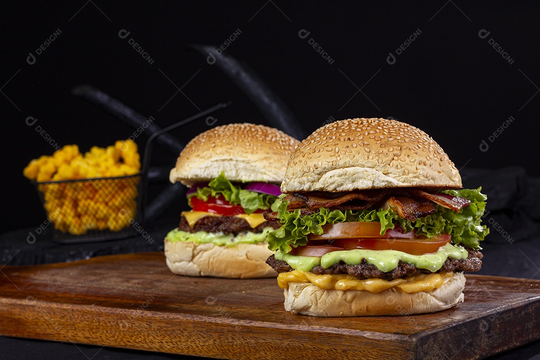 Dois hamburgueres sobre tábua de madeira e cestinha de batata frita