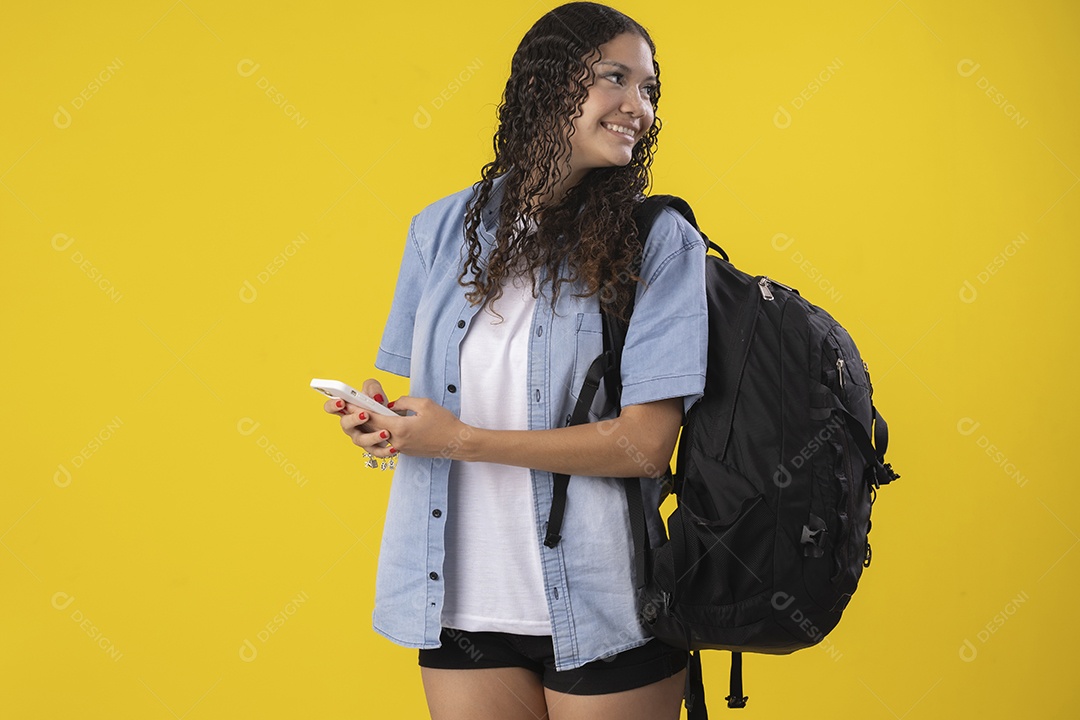 Jovem com camiseta jeans bolsa na costas e um celular nas mãos