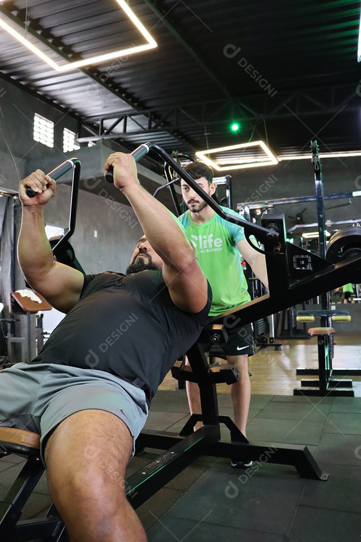 Belo personal trainer ajudando homem executar exercícios sobre uma academia