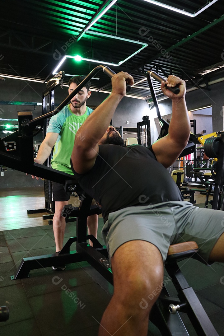 Belo personal trainer ajudando homem executar exercícios sobre uma academia