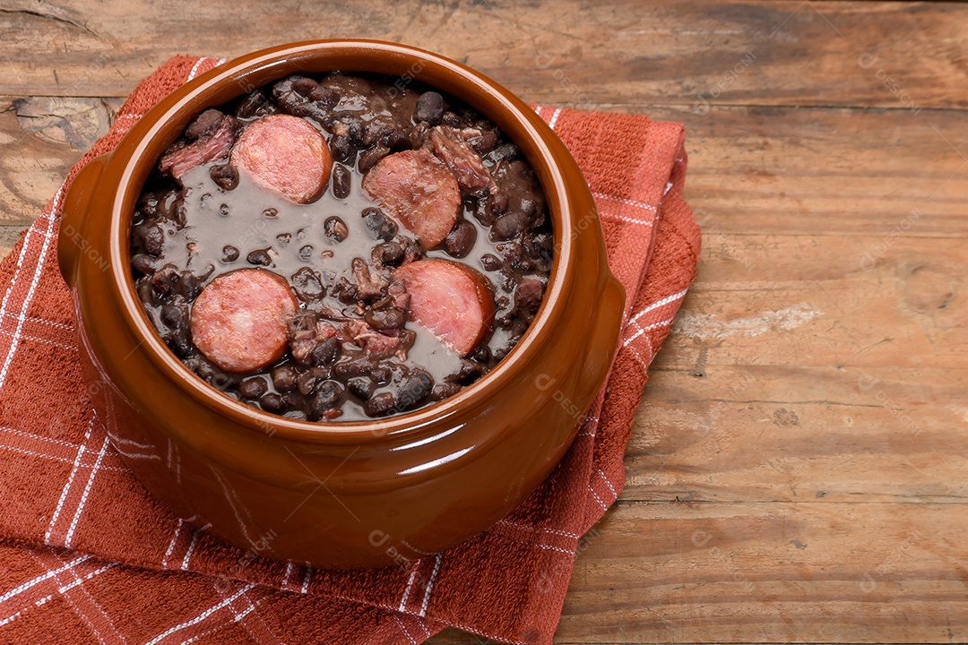 Panela cheia de feijoada sobre mesa de madeira