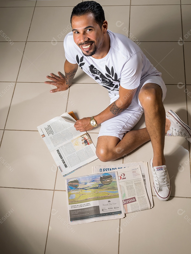 Um adoravél homem sentado no chão lendo jornais