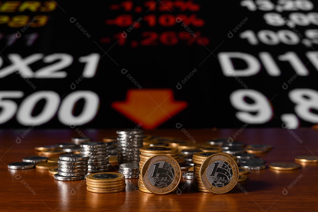 Várias moedas de um real e cinquenta centavos sobre mesa de madeira