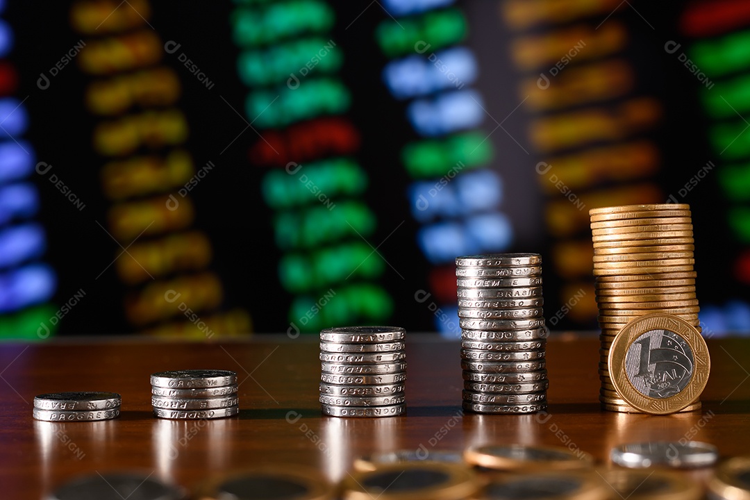 Cinquenta centavos e moedas de um real empilhadas sobre uma mesa