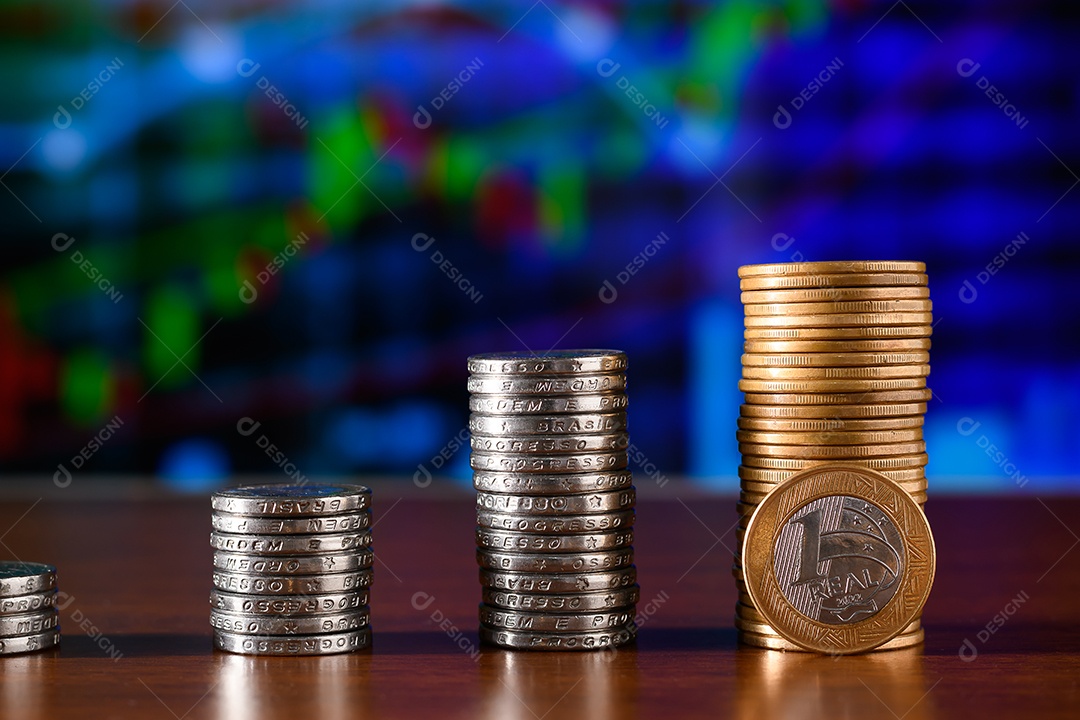 Cinquenta centavos e moedas de um real empilhadas sobre uma mesa