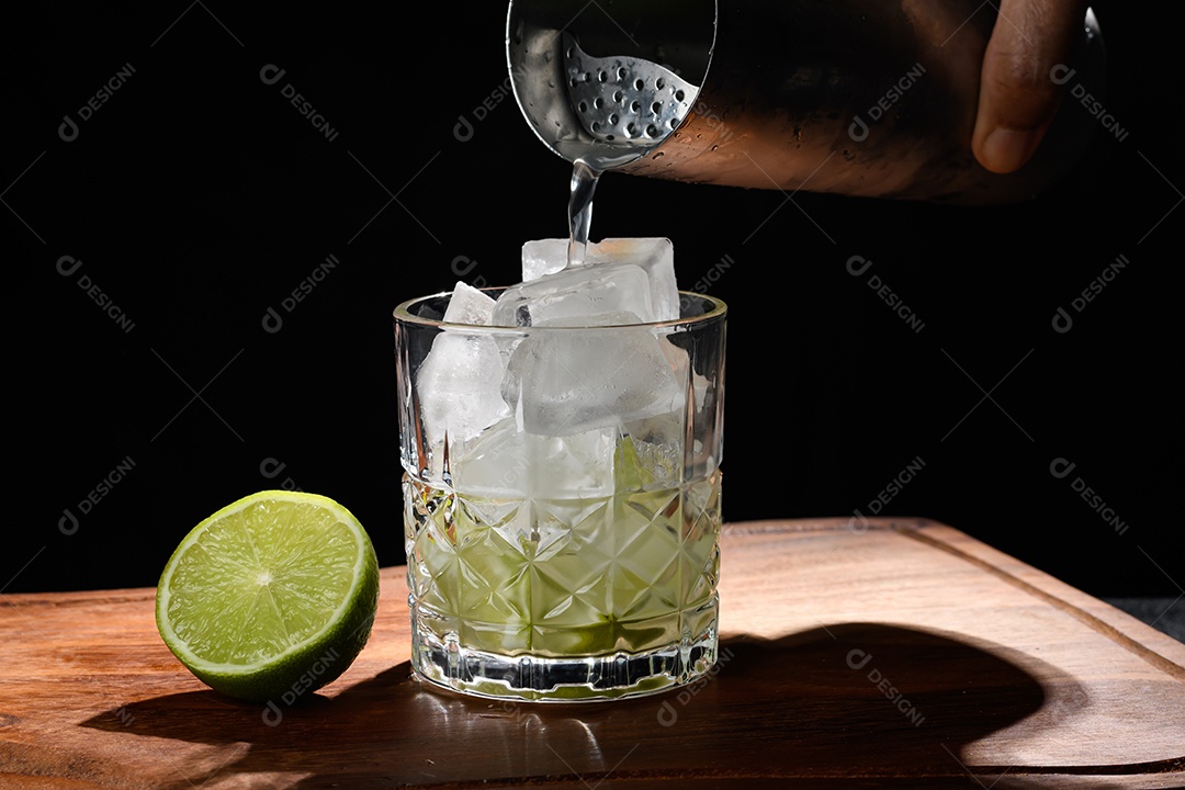 Mão colocando alcóol e suco de limão na caipirinha