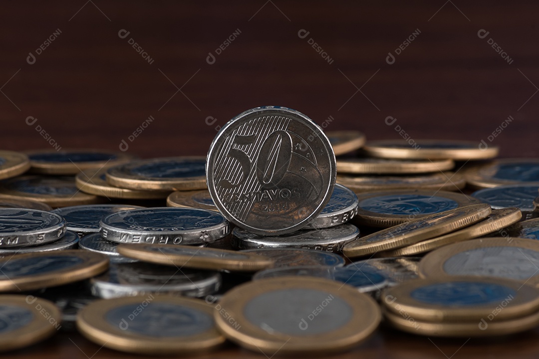 Moedas de um real e cinquentas centavos sobre uma mesa de madeira