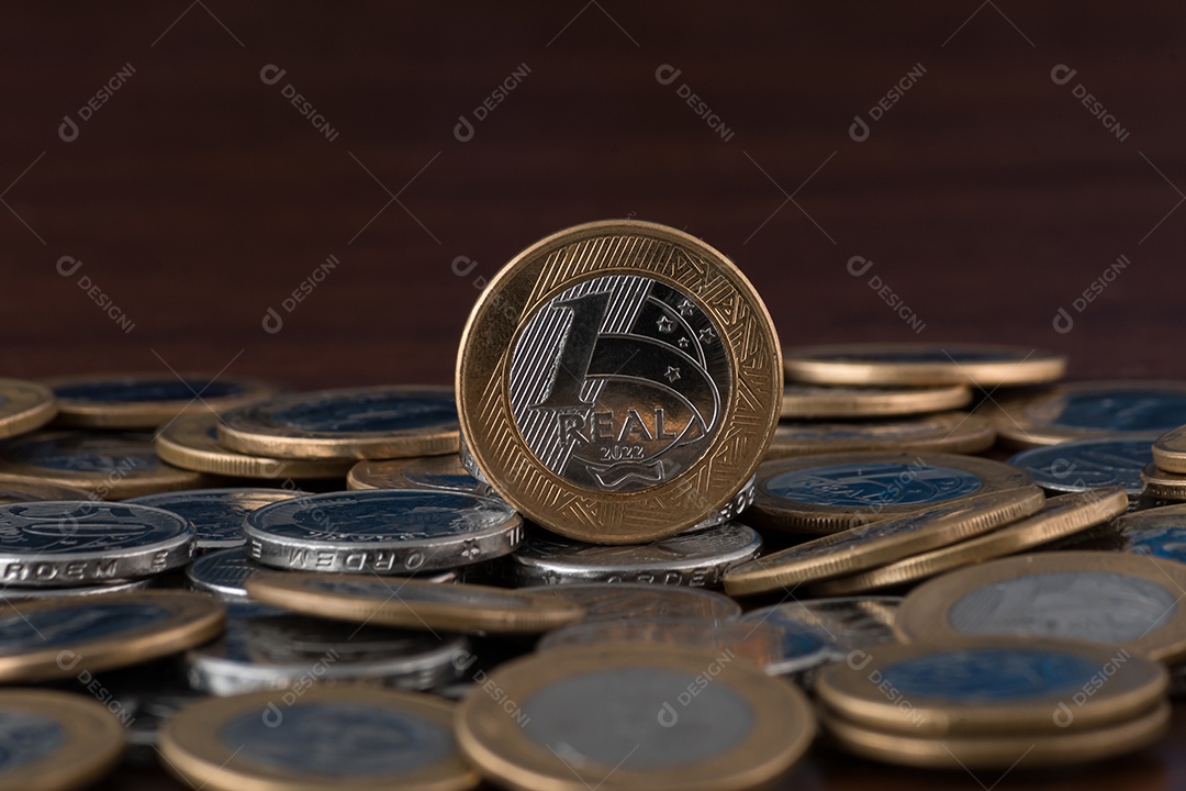 Moedas de um real e cinquentas centavos sobre uma mesa de madeira
