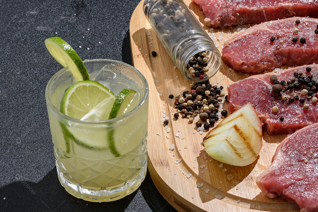 Tábua com carne temperada e um copo de caipirinha churrasco