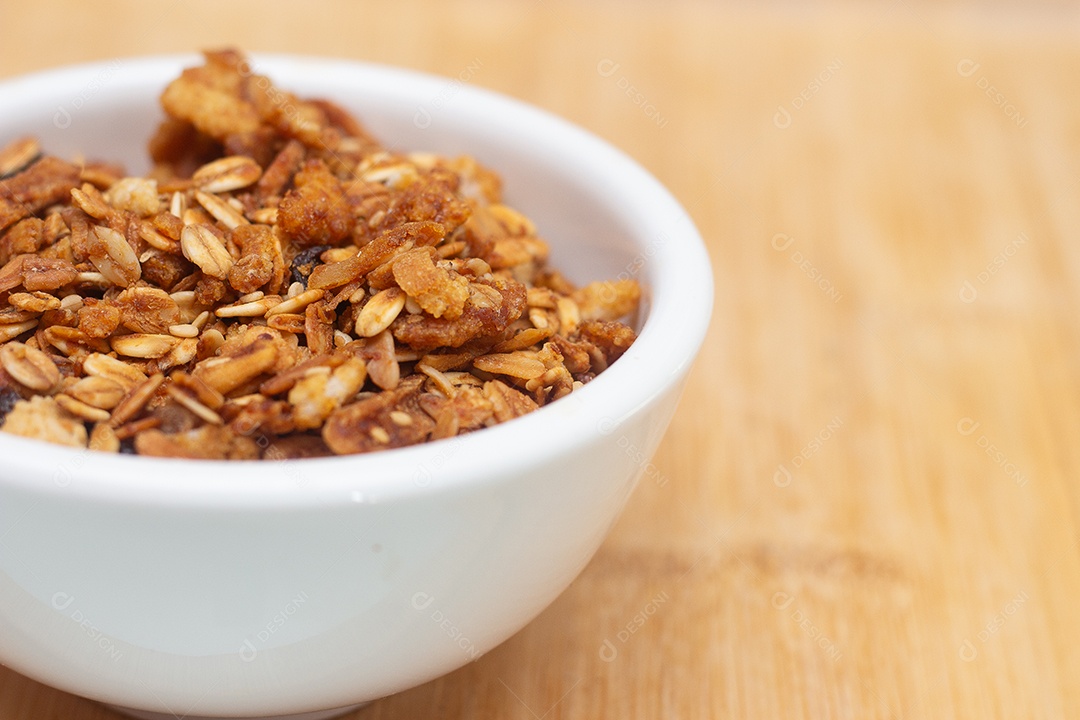 Tigela branca cheia de granola sobre uma mesa de madeira