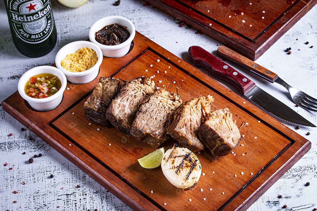 Carne assada sobre tábua de madeira com molho vinagrete farofa